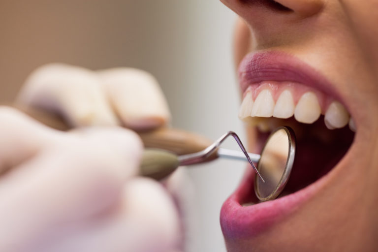 Close-up of dentist examining a female patient with tools at dental clinic